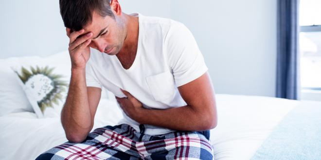 A man sitting on his bed with stomach discomfort.