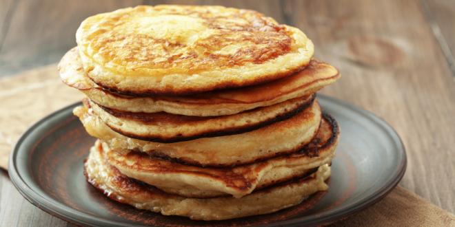 A stack of pancakes on a grey pottery plate placed on a wooden table.