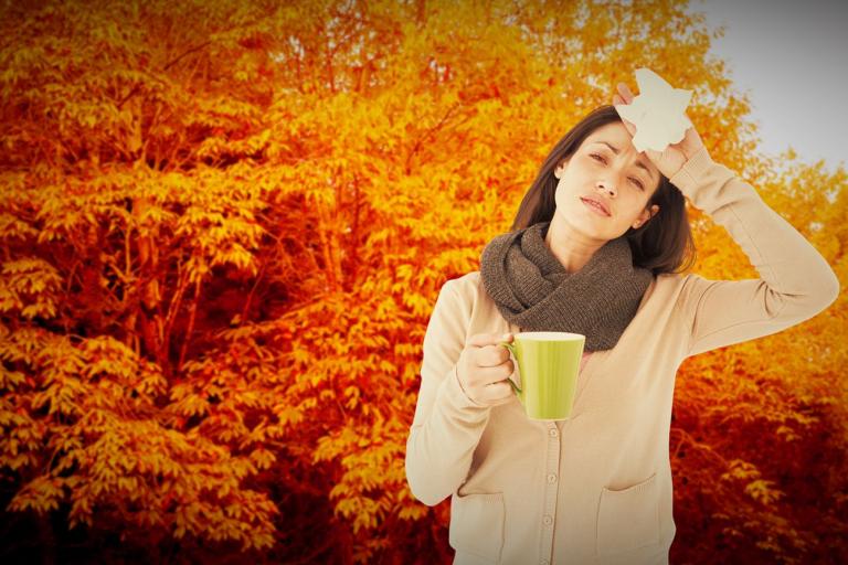 A sick woman holding a mug and a tissue in autumn